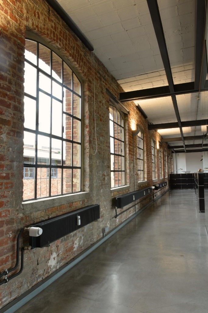 Long corridor with a brick wall, arched windows and a concrete floor