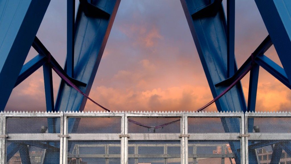 Blue steel struts of a crane against a pink evening sky