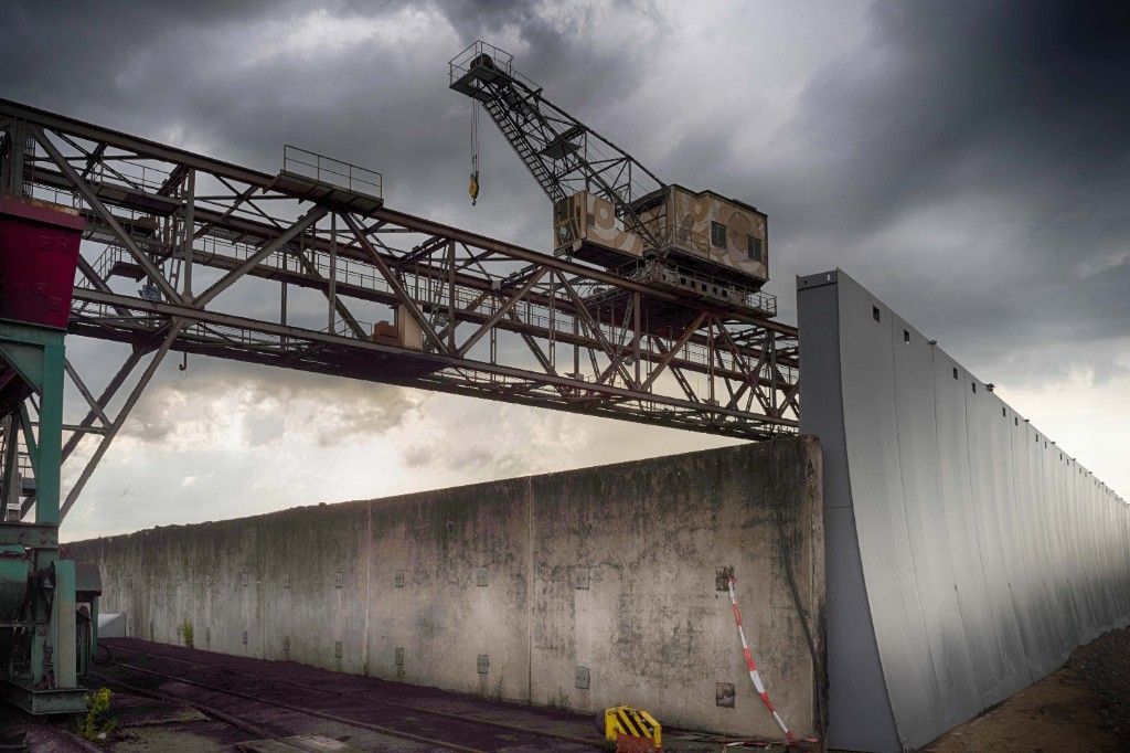 Old gantry crane over rails beside a concrete wall under storm clouds