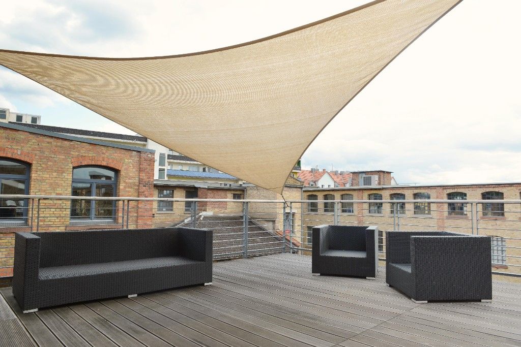 Roof terrace with a sun sail and lounge furniture between brick buildings