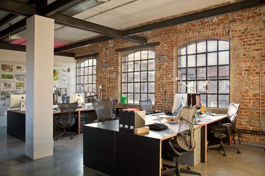 Desks with monitors and office chairs below arched windows