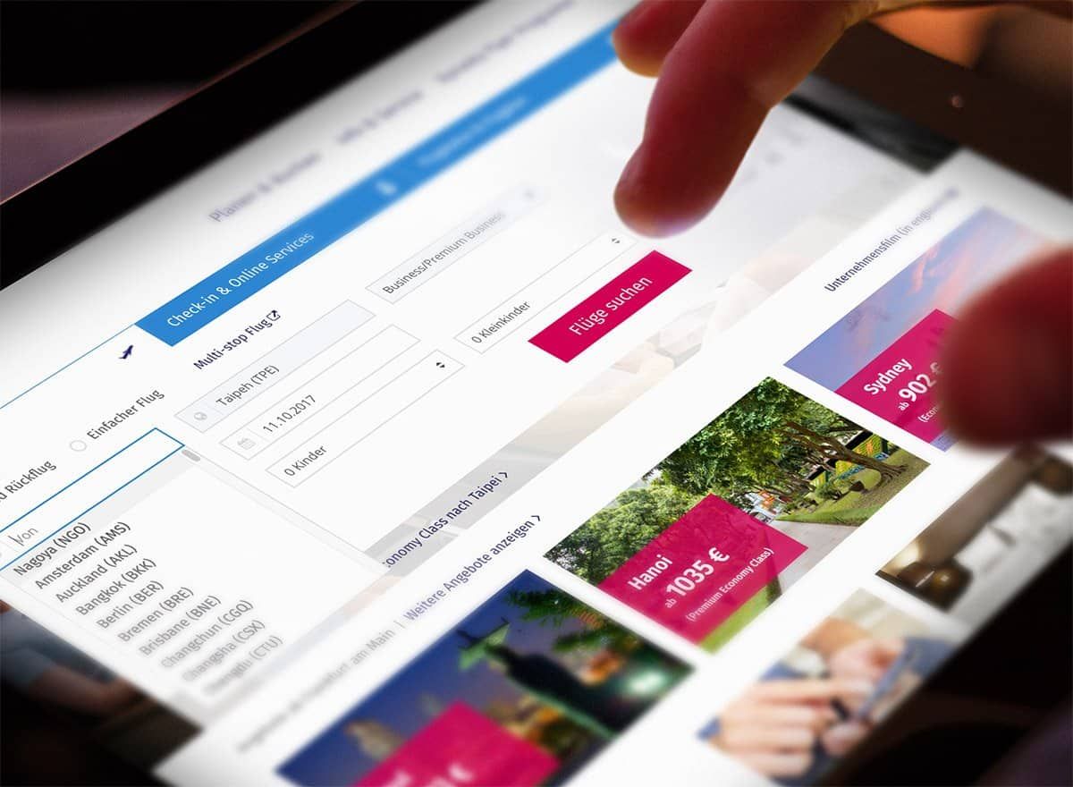 A finger tapping the flight search of the website on a tablet, with offers to Hanoi and Sydney beside it