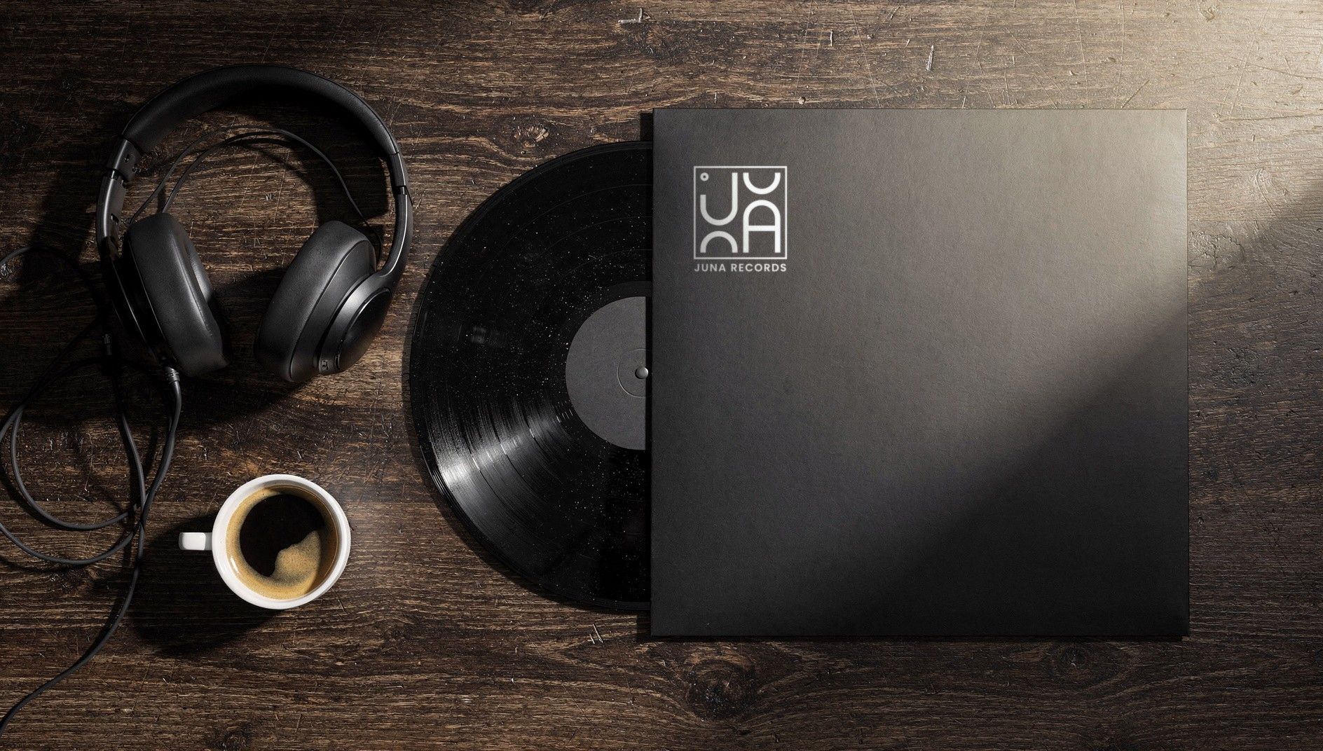Black record sleeve with the white JUNA RECORDS logo on a dark wooden table, next to a vinyl record, headphones and an espresso