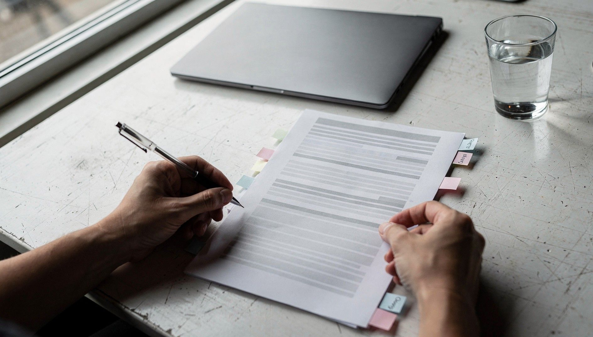 Two hands working through a printed policy with highlighted lines and tabs along the edge