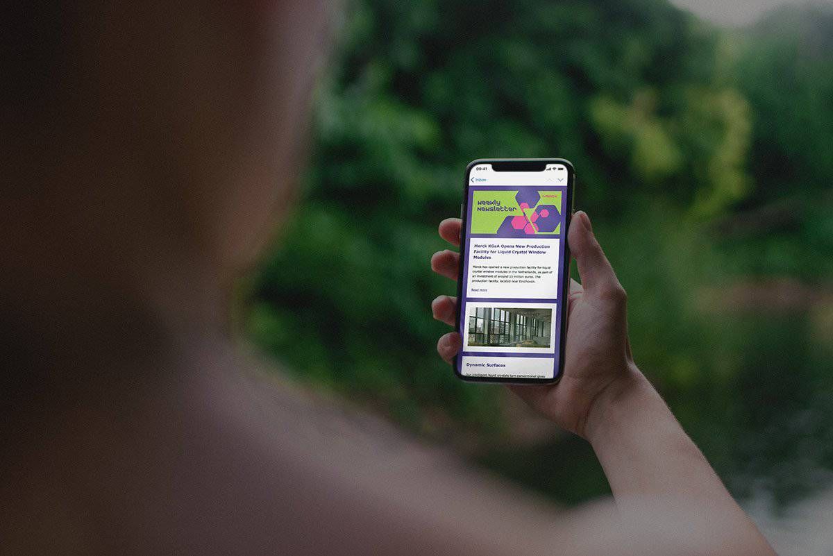 Hand holding a smartphone showing the Merck KGaA Weekly Newsletter
