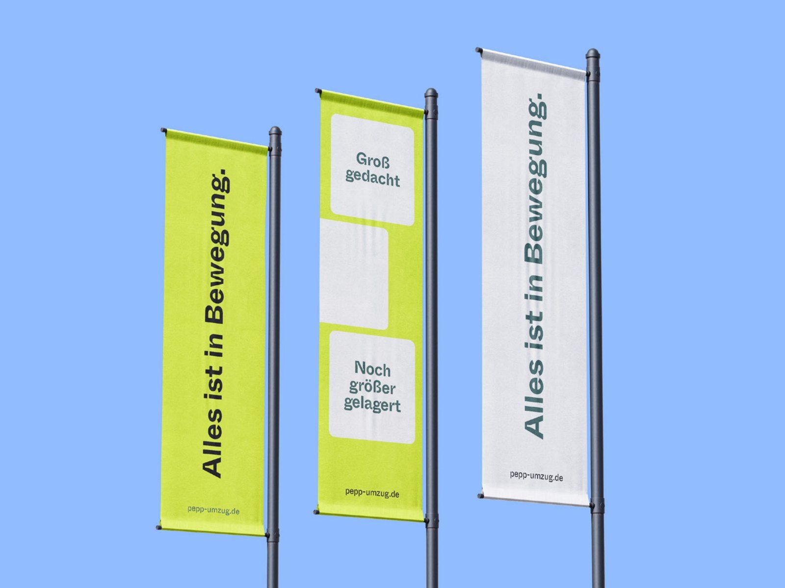 Three flags on poles, two in lime and one in white, reading “Alles ist in Bewegung.” and “Groß gedacht. Noch größer gelagert.”