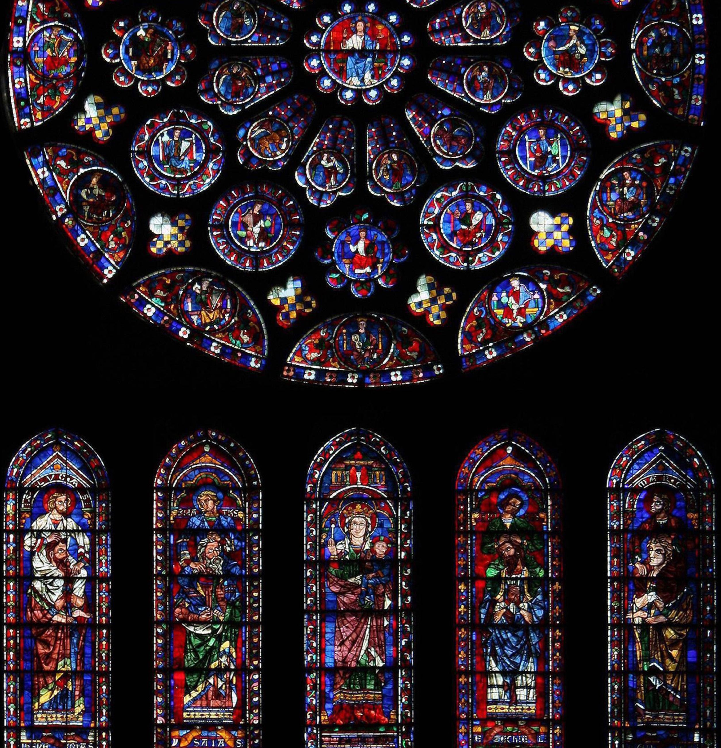 The great rose window in the south transept at Chartres, with five tall, narrow windows of figures in glowing glass beneath it
