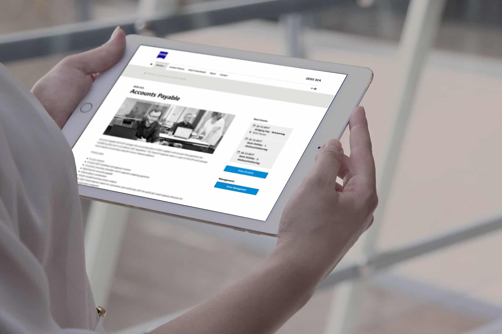 Hands holding a tablet showing the Accounts Payable page of the Carl Zeiss AG Shared Service Center intranet